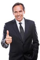 Good job Confident mature man in formalwear looking at camera and smiling while showing his thumb up and standing against white background photo