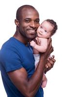 mi bebé feliz joven africano sosteniendo a su pequeño bebé y sonriendo mientras está de pie aislado en blanco foto