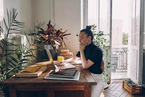 mujer joven confiada que usa una computadora portátil mientras está sentada en su lugar de trabajo en la oficina foto