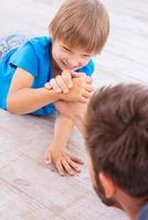 I am winning Top view of father and son competing in arm wrestling while both lying on the hardwood floor photo