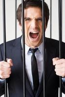 I am not guilty Furious young man in formalwear standing behind a prison cell and shouting photo
