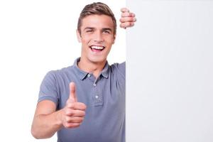Thumb up Happy young man looking at camera and showing his thumb up while leaning at the copy space and standing against white background photo