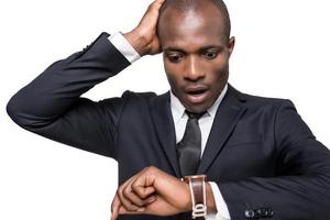 Late again Worried young African man in formalwear checking time while looking at his watch and standing isolated on white background photo