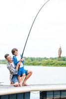 It is a big fish Father and son stretching a fishing rod with fish on the hook photo