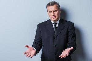 What is that Displeased mature man in formalwear gesturing and looking away while standing against grey background photo