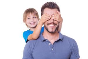 Guess who Playful little boy covering his father eyes with hands and smiling while both standing isolated on white background photo