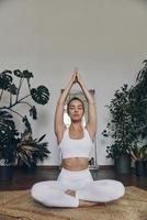 mujer joven relajada meditando mientras se sienta en el suelo con plantas de interior a su alrededor foto