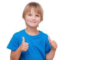 pulgares arriba alegre niño mostrando sus pulgares hacia arriba y sonriendo mientras está de pie aislado en blanco foto