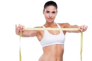 Stay fit Attractive young woman in white bra and panties showing measuring tape and smiling while standing isolated on white photo