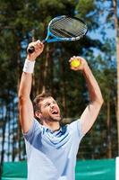 I am a winner Happy young man in polo shirt raising his tennis racket up while standing on tennis court photo