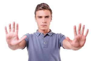 Stop it Serious young man stretching out hands and showing his palms while standing isolated on white background photo