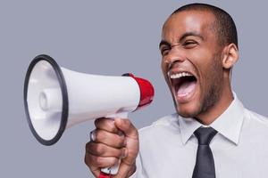 Can you hear me now Furious young African man in formalwear shouting at megaphone while standing against grey background photo