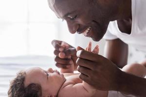 You are my world Side view of happy young African man playing with his little baby and smiling while lying in bed photo