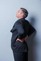 Good idea Thoughtful mature man in formalwear pointing up while standing against grey background photo