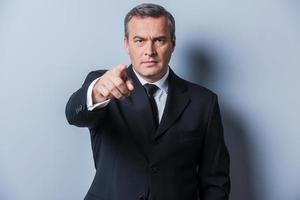 You are the next Confident mature man in formalwear pointing you while standing against grey background photo