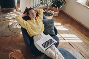 Top view of happy young woman using laptop while sitting in a comfortable chair at home photo