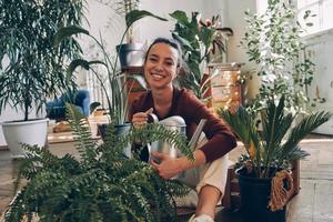 mujer joven feliz sosteniendo una lata de agua mientras se sienta en el suelo con plantas de interior foto