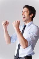 I did it Side view of excited young man in shirt and tie gesturing and smiling while standing against grey background photo