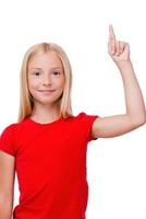 Look over there Cheerful little girl pointing up and looking at camera while standing isolated on white photo