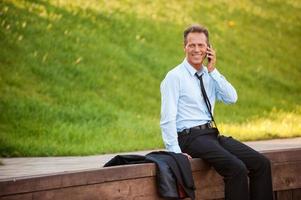 Businessman in nature. Confident mature businessman talking on the mobile phone and smiling while sitting at the quayside photo