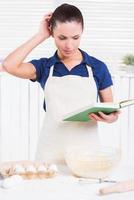 What am I doing wrong Cheerful young woman in apron holding rolling pin and wire whisk while standing in a kitchen photo