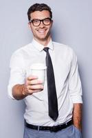 Refresh your mind Confident young man in shirt and tie stretching out coffee cup and smiling while standing against grey background photo