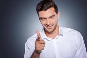 I choose you Handsome young man in white shirt looking at camera and pointing you while standing against grey background photo