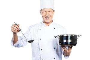 Deberías probar esta sopa. chef maduro alegre con uniforme blanco sosteniendo cazuela y cuchara mientras se enfrenta a fondo blanco foto