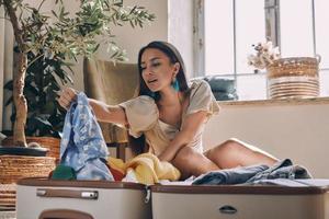 Beautiful young woman unpacking suitcase while sitting on the floor at home photo