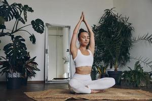 Attractive young woman meditating while sitting on the floor with houseplants all around her photo