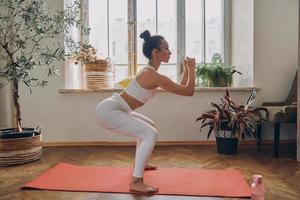 Confident woman standing in squatting position while practicing in front of the window at home photo