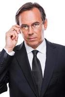 How may I help you Portrait of confident mature man in formalwear adjusting his eyeglasses and looking at camera while standing against white background photo