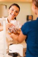 Here you go Beautiful young female baker giving cookies to customer and smiling photo