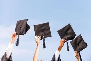 Finally graduated Close-up of four hands holding mortar boards against sky background photo