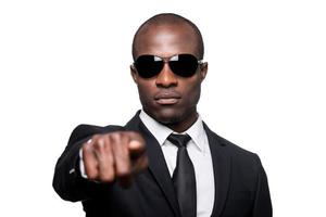 You the next Serious young African man in formalwear and sunglasses pointing you while standing isolated on white background photo