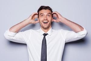 It is just unbelievable Happy young man in shirt and tie touching head with hands and smiling while standing against grey background photo