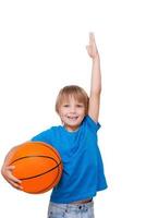 quiero ser un niño alto y alegre sosteniendo una pelota de baloncesto y gesticulando mientras estoy aislado en blanco foto