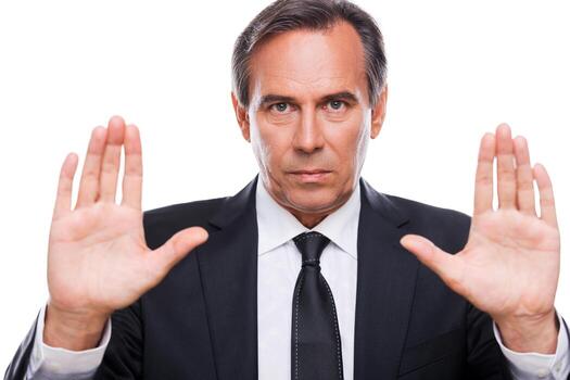 Stop it Serious mature man in formalwear looking at camera and showing his palms while standing isolated on white background photo