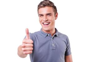 Thumb up Happy young man looking at camera and showing his thumb up while standing isolated on white background photo