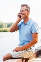 I am so glad to hear you Side view of happy mature man talking on the mobile phone and smiling while sitting at the quayside photo