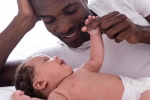 You are my everything Side view of happy young African man playing with his little baby and smiling while lying in bed photo