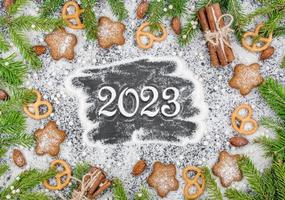 Feat lay Christmas background with cookies, fir branches and sweets. New Year 2023 lettering powdered sugar photo