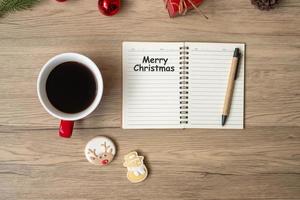 cuaderno, taza de café negro, galletas navideñas y bolígrafo sobre mesa de madera, vista superior y espacio para copiar. navidad, feliz año nuevo, metas, resolución, lista de tareas, estrategia y concepto de plan foto