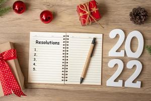2022 resoluciones con cuaderno, regalo de navidad y bolígrafo sobre mesa de madera. navidad, feliz año nuevo, objetivos, lista de tareas, inicio, estrategia y concepto de plan foto