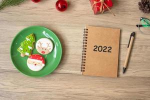 Cuaderno 2022, negro, galletas navideñas y bolígrafo sobre mesa de madera, vista superior y espacio para copiar. navidad, feliz año nuevo, objetivos, resolución, lista de tareas, estrategia y concepto de plan foto