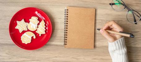 Woman hand writing on notebook with Christmas cookies on table. Xmas, Happy New Year, Goals, Resolution, To do list, Strategy and Plan concept photo