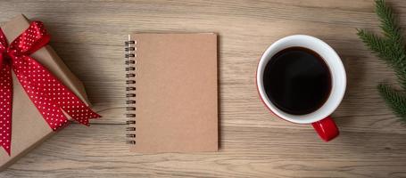 Blank notebook, black coffee cup and Christmas gift on wood table, Top view and copy space. Xmas, Happy New Year, Goals, Resolution, To do list, Strategy and Plan concept photo