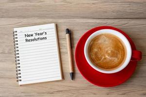 resolución de año nuevo con cuaderno, taza de café negro y bolígrafo sobre mesa de madera. navidad, feliz año nuevo, metas, lista de tareas, estrategia y concepto de plan foto