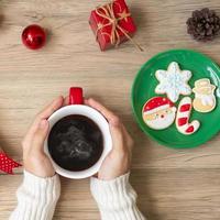 Merry Christmas with woman hand holding coffee cup and homemade cookie on table. Xmas eve, party, holiday and happy New Year concept photo