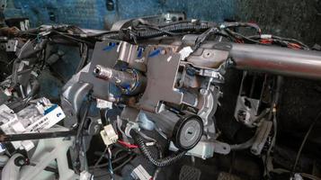 interior or dashboard of a car that is being disassembled or repaired, the steering column frame, shift lever, and interior cables are visible photo